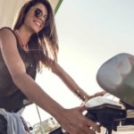 A smiling woman puts fuel into her car at a petrol pump.