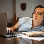 A young woman slumped in her chair while looking at her laptop.