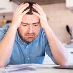 A worried man holds his head and look at his computer.