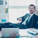 A man in a suit plays air guitar at his desk like a boss.