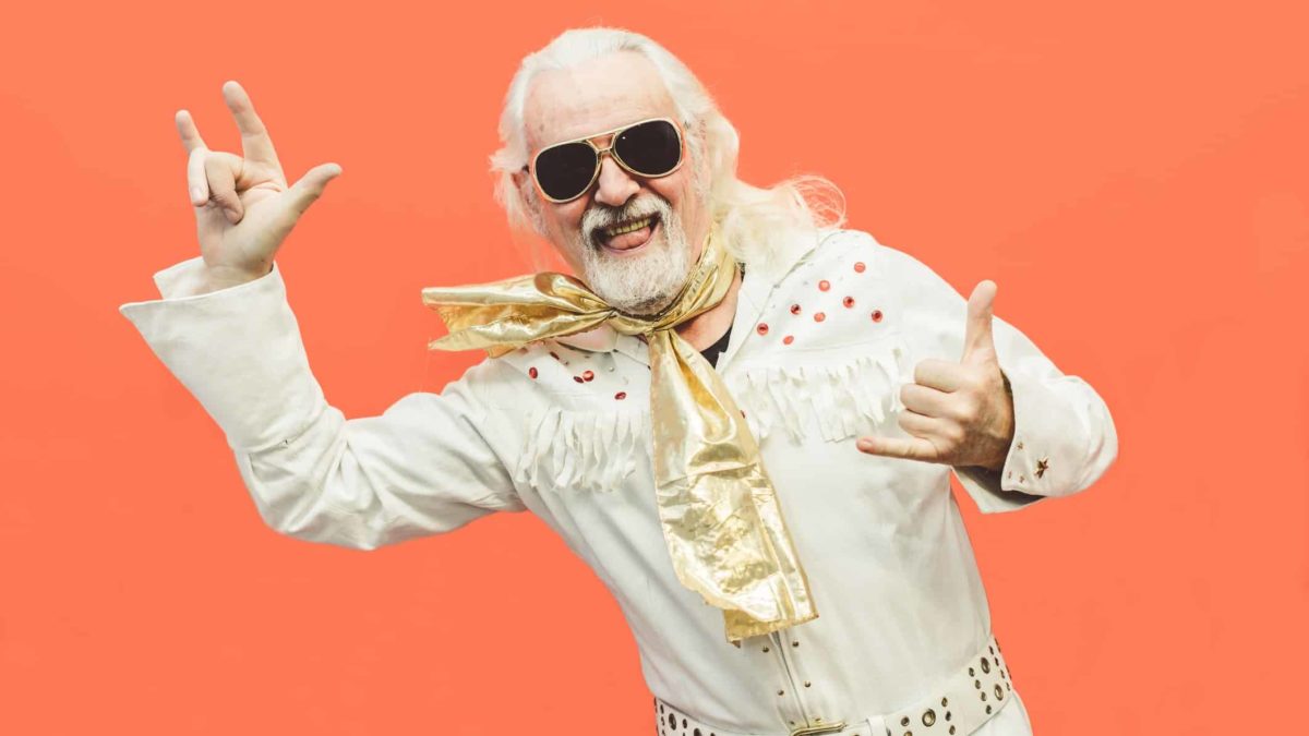 An older man with white hair in an Elvis-style white suit rocking out.