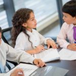 Three young people in business attire sit around a desk and discuss.