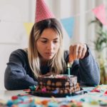 A woman stares at the candle on her cake, her birthday has fizzled.