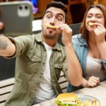 A couple makes silly chip moustache faces and take a selfie on their phone.