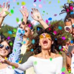 A group of friends party and dance in the desert with colourful confetti all around them.