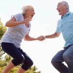 An older couple hold hands as they bounce happily high in the air.
