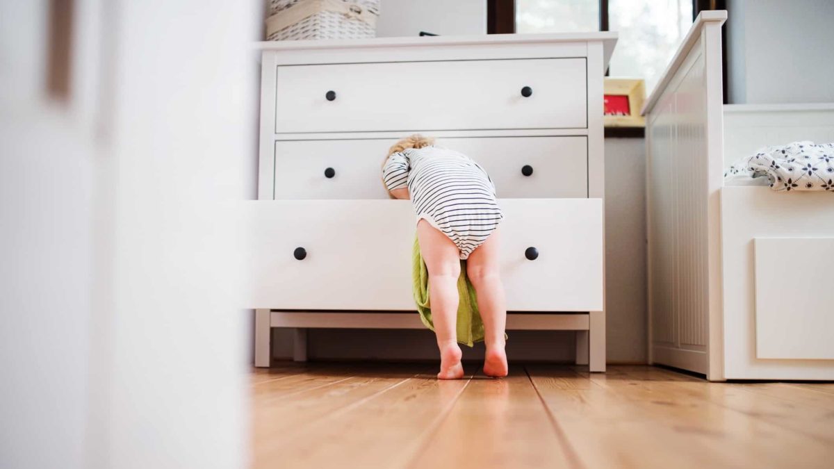 A baby reaches into the bottom drawer of a chest of drawers.