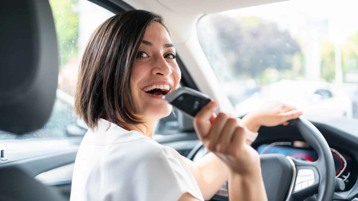 A woman smiles over her shoulder as she sits in the driver's seat of a car with keys in hand.