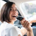 A woman smiles over her shoulder as she sits in the driver's seat of a car with keys in hand.