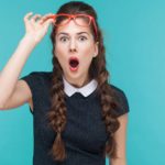 A young woman lifts her red glasses with one hand as she takes a closer look at news about interest rates rising and one expert's surprising recommendation as to which ASX shares to buy