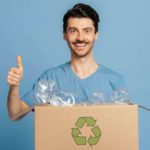 A man holding a packaging box with a recycle symbol on it gives the thumbs up.