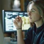 A woman sits in front of a computer and does some calculations.