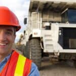 Miner standing in front of trucks and smiling, symbolising a rising share price.