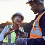 Two young African mine workers wearing protective wear are discussing coal quality while on site at a coal mine.