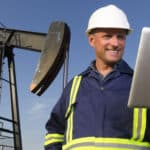 An oil worker in front of a pumpjack using a tablet PC.