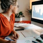 Business women working from home with stock market chart showing per cent change on her laptop screen.