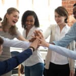 A diverse group of happy office workers join hands in a team high five in celebration of a job well done.