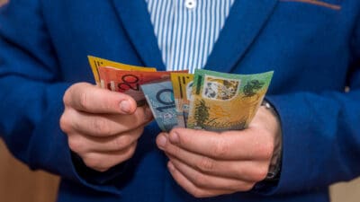 Male hands holding Australian dollar banknotes, symbolising dividends.