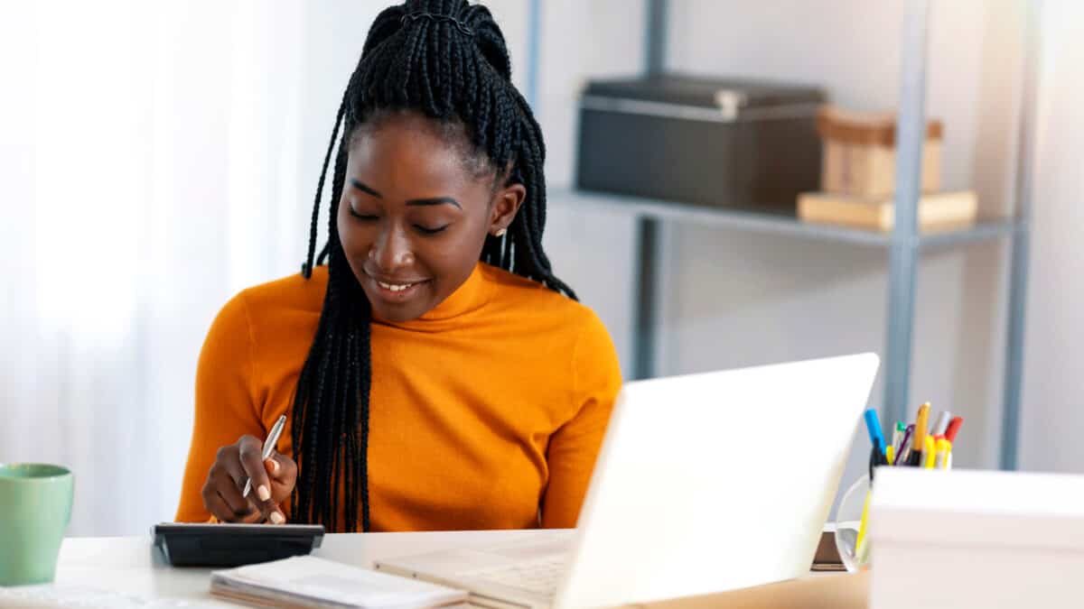 Primo piano di una donna che utilizza calcolatrice e laptop per calcolare i guadagni.