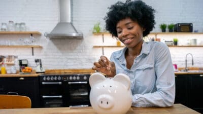 Woman at home saving money in a piggybank and smiling.