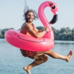 Man jumping in water with a floatable flamingo, symbolising passive income.