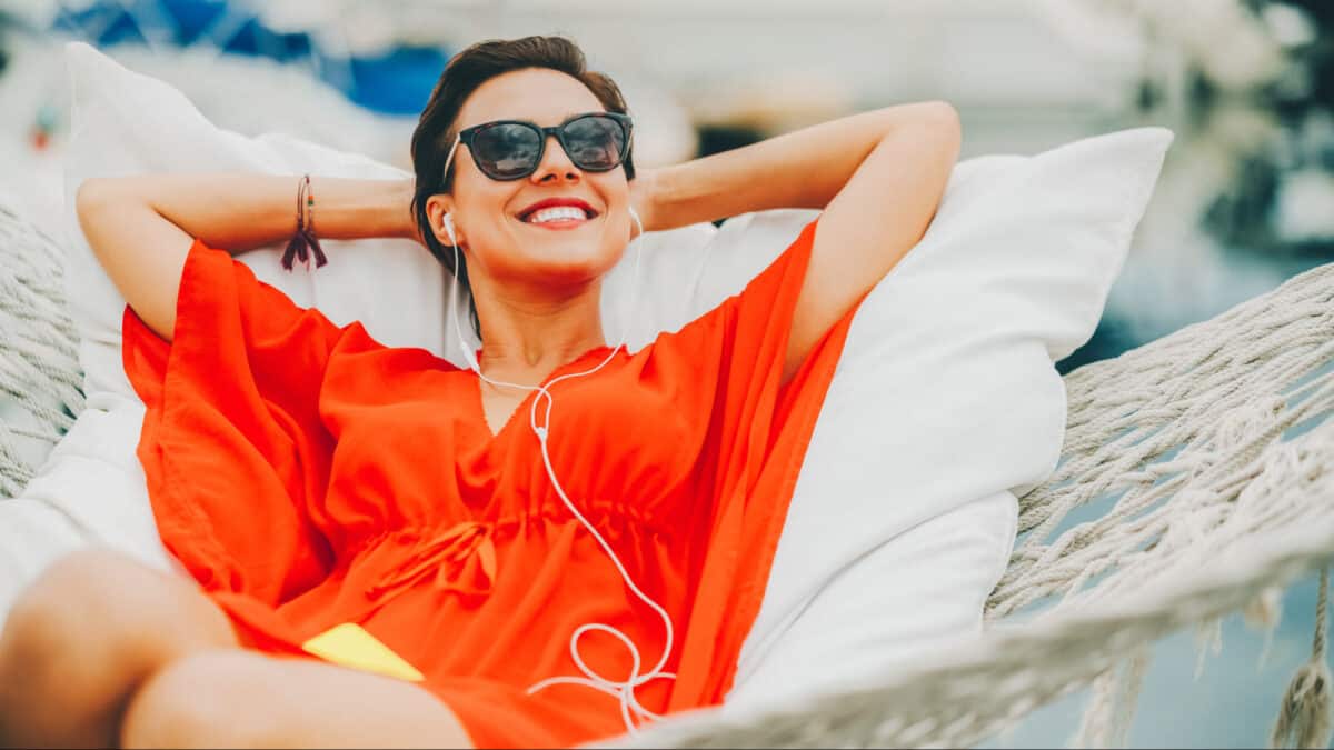 A woman in hammock with headphones on enjoying life which symbolises passive income.