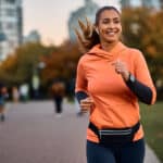 Young happy athletic woman listening to music on earphones while jogging in the park, symbolising passive income.