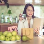 Woman with a coffee mug in one hand and a tablet in another along with pears on the table, symbolising inflation.