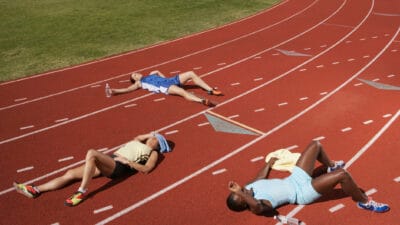 Three women athletes lie flat on a running track as though they have had a long hard race where they have fought hard but lost the event.