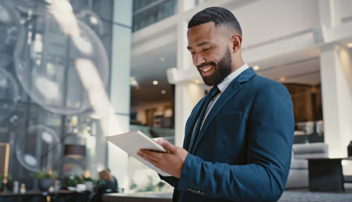 A businessman looking at his digital tablet or strategy planning in hotel conference lobby. He is happy at achieving financial goals.