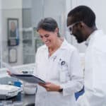 In the lab at work, the mature adult woman and young adult man smile as they review the results of their successful experimentation.