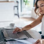 Young businesswoman sitting in kitchen and working on laptop.