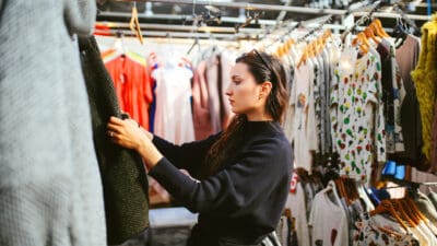 Vintage toned portrait of a young beautiful brunette woman in London second hand marketplace. She is wearing casual clothes, black knitted sweater, looking through the second hand market stalls.