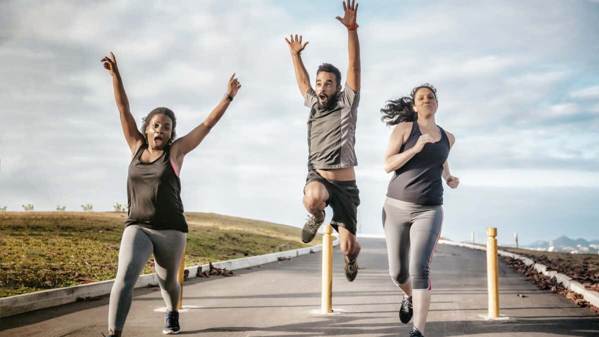 Three exuberant runners dash towards the camera. One raises her arms in triumph; another jumps in the air with arms raised. The third runner gives a satisfied smile.