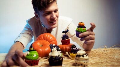 A smiling young man presents a selection of cupcakes decorated as spooky treats for the Halloween trick or treat tradition