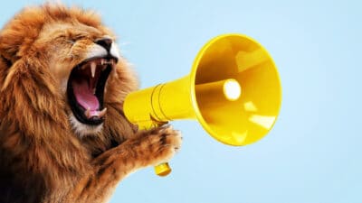 Lion holding and screaming into a yellow loudspeaker on a blue background, symbolising an announcement from Liontown.