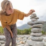 A young woman carefully adds a rock to the top of a pile of balanced river rocks.