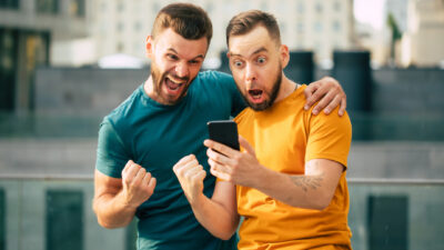 Two happy excited friends in euphoria mood after winning in a bet with a smartphone in hand.