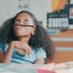 A young girl looks up and balances a pencil on her nose, while thinking about a decision she has to make.