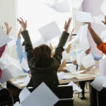 Smiling office workers fling a stack of papers into the air.