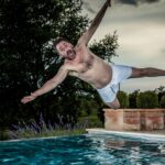 A man with arms spread yells as he plunges into a swimming pool.