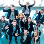 Ten smiling business people wave to the camera after receiving some winning company news.