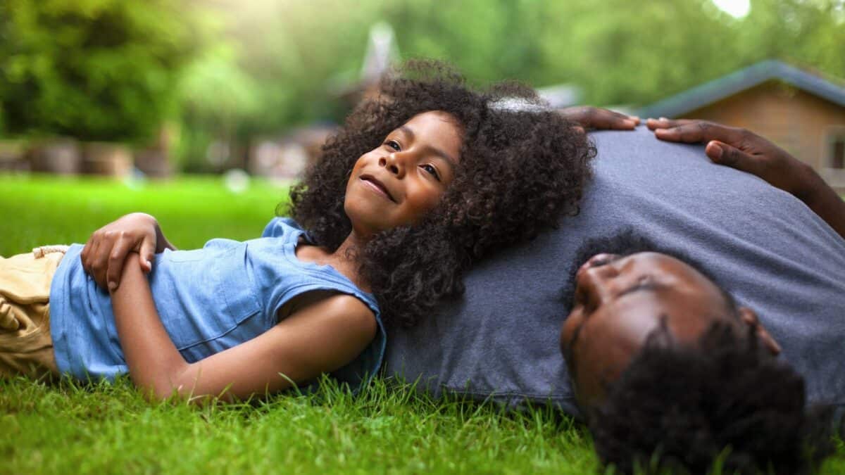 A happy young girls lies in the grass with her father, smiling at the prospects of a bright future.