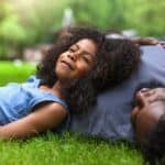 A happy young girls lies in the grass with her father, smiling at the prospects of a bright future.