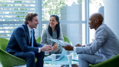 Three happy multi-ethnic business colleagues discuss investment or finance possibilities in an office.