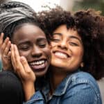 Two close female friends hug each other and smile after receiving good news.