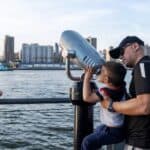 A father helps his son look through binoculars during a family holiday or day out in the city.