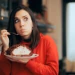 A rueful woman tucks into a sweet pie as she contemplates a decision with regret.