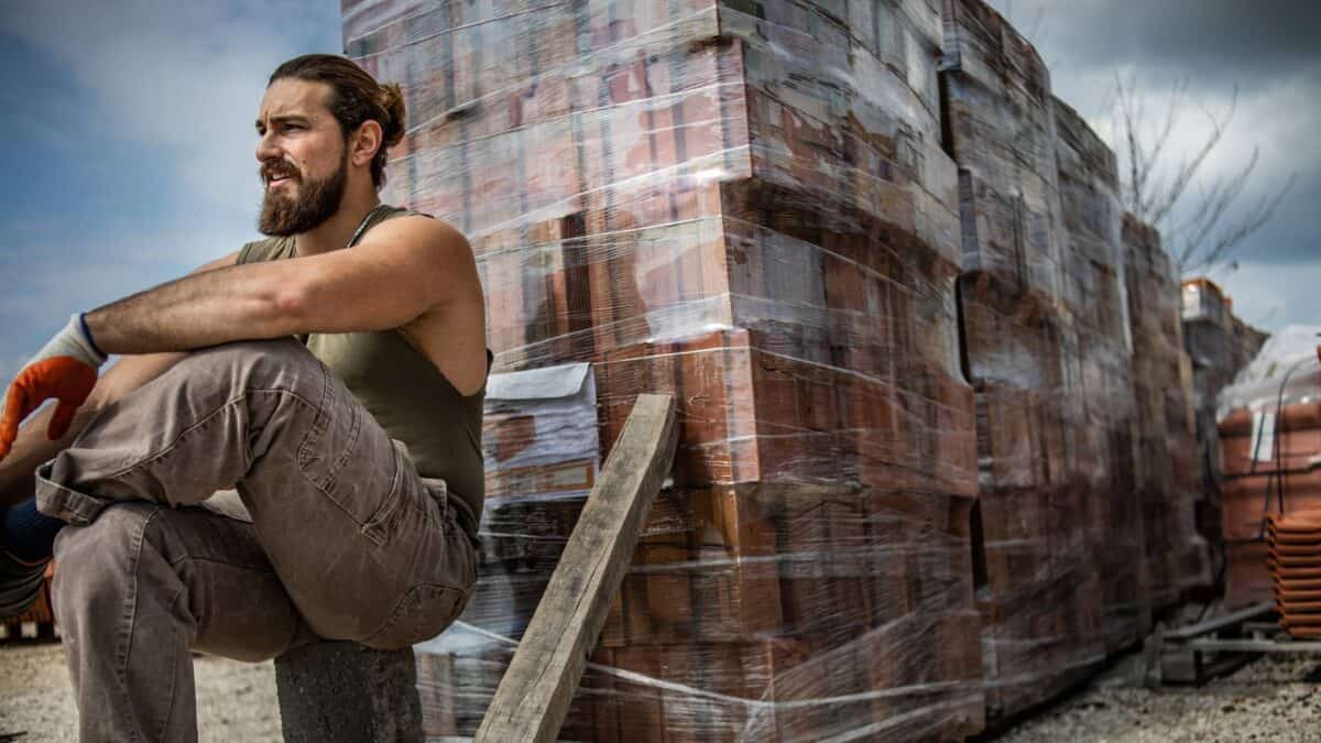 A brickie sits next to a pile of bricks all stacked up and ready to lay.