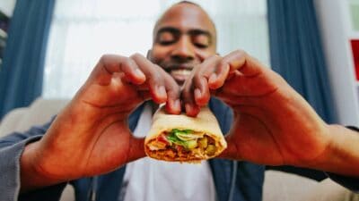 A smiling man take a big bite out of a burrito